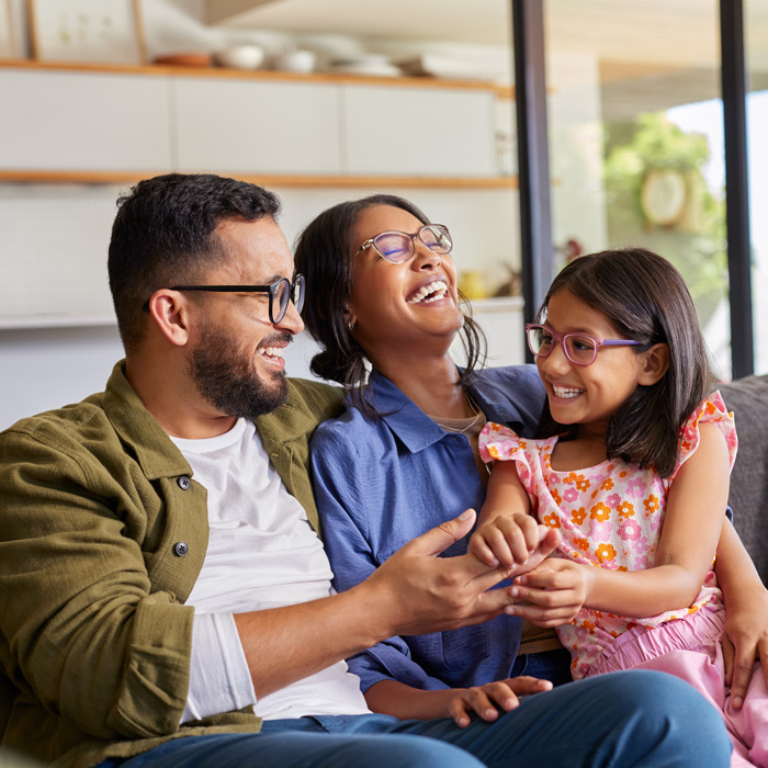 laughing family of three sitting on couch at home